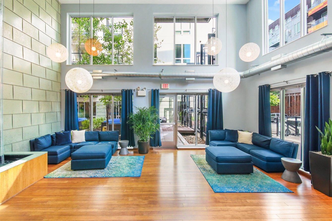 Modern communal lounge area with blue sectionals, ottoman, and decorative pendant lights.