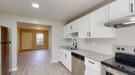 Located at 4603 Elcone Dr in Fayetteville, North Carolina, this single-floor home offers a clean, updated interior with a cohesive neutral palette and light wood-style flooring that flows consistently throughout the space. The kitchen serves as a standout feature, outfitted with crisp white shaker-style cabinetry accented by matte black hardware, granite countertops with subtle veining, a modern pull-down faucet, a stainless steel dishwasher, and a stainless steel electric range with a ventilation hood above. A secondary door in the kitchen provides convenient exterior access with natural light filtering through its window. The open layout connects the kitchen to the main living area, creating an easy, functional flow. The bedrooms are well-proportioned with neutral walls and textured ceilings, and at least one bedroom includes a closet with built-in shelving for storage. The bathroom features marble-look tile in the walk-in shower, a granite-topped vanity with an undermount sink, and a lighted mirror. A dedicated laundry area with washer and dryer connections is also present. Throughout the home, clean white baseboards and a consistent finish create a polished, move-in-ready atmosphere.