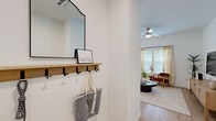 Located at 5901 Myrtle Dr in Wildwood, Florida, this efficiently designed single-floor home offers a thoughtful layout across one bedroom and one bathroom. The entrance welcomes you with a practical mudroom-style foyer complete with a wall-mounted shelf, coat hooks, and a mirror — a functional first impression that sets the tone for the rest of the home.

The open living room features light hardwood-style flooring, high ceilings, a ceiling fan, and large windows dressed with sheer curtains that invite an abundance of natural light. The space flows naturally into the kitchen, which is outfitted with crisp white shaker cabinetry, white quartz countertops, stainless steel appliances including a refrigerator, dishwasher, and microwave, and a central island with bar seating. A sliding glass door provides outdoor views and additional light.

The bedroom is a comfortable retreat with multiple windows, a ceiling fan, and a built-in closet. The full bathroom includes a tiled tub-shower combination, a single vanity with white cabinetry, and a window for natural ventilation. Consistent light hardwood-style flooring and a neutral white palette unify the home, creating a clean, modern aesthetic throughout.