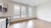This efficiently designed one-bedroom, one-bathroom unit makes excellent use of its compact footprint, offering a thoughtfully laid-out single-floor living space. The open living area is bright and airy, featuring light hardwood-style flooring and a generous bank of three large windows dressed with horizontal blinds, allowing ample natural light to fill the room.

The kitchen is a standout feature, showcasing gray shaker-style cabinetry, a white subway tile backsplash, and sleek light countertops. A full suite of stainless steel appliances — including a refrigerator, range, built-in microwave, and dishwasher — provides a modern, functional cooking space. An open shelf adds a contemporary touch alongside the upper cabinetry.

The bedroom offers plush neutral carpet flooring and vaulted ceiling angles that lend a sense of added openness. A built-in closet with a wire shelving system provides practical storage, and the room's clean white walls create a calm, restful atmosphere.

The bathroom is finished with large-format tile flooring in a neutral tone and features a soaking tub with a full subway-tiled surround, a curved shower rod, and brushed nickel hardware and grab bar accents, giving it a clean and polished look. Overall, the unit presents a fresh, modern aesthetic with consistent finishes throughout.