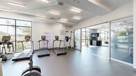 Located at 505 W 31st St in Los Angeles, California, this modern fitness center offers a comprehensive and thoughtfully designed exercise facility across a single, open floor. The space is characterized by a clean, contemporary aesthetic with a neutral color palette, coffered white ceilings, and recessed linear lighting that creates a bright and energizing atmosphere throughout.

The main exercise area accommodates a wide range of workout equipment, including a row of treadmills, cable machines, weight benches, and free weights, providing ample room for both cardio and strength training. A dedicated functional training zone features a full rack of accessories including kettlebells, resistance bands, medicine balls, and stability equipment, organized on wall-mounted shelving beneath a striking mountain landscape mural that adds a calming, artistic focal point to the space.

A separate cycling area benefits from floor-to-ceiling glass walls that invite abundant natural light and offer views of the surrounding Los Angeles streetscape, including mature palm trees — bringing an outdoor ambiance to indoor workouts. Frosted glass sliding doors divide the zones while maintaining an open, connected feel. The space also includes a wall-mounted television, a water station, and durable rubber flooring throughout, ensuring both functionality and comfort for all types of training.