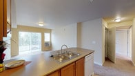 This single-floor residence offers a practical and comfortable layout designed for everyday living. The kitchen is equipped with white appliances including a coil-burner range, over-the-range microwave, refrigerator, and dishwasher. Warm-toned wood cabinetry provides ample storage, while a peninsula with a double stainless steel sink and laminate countertops connects the kitchen to the adjacent living area. The kitchen features light hardwood-style flooring, which transitions to plush wall-to-wall carpeting throughout the living and bedroom areas. The open living space is bright and generously sized, with a sliding glass door that offers access to an outdoor area and allows natural light to filter in. Two bedrooms feature large windows with vertical blinds, baseboard heating, and soft carpeting, creating comfortable retreats. One bedroom includes a walk-in closet and direct access to an en-suite bathroom. Both bathrooms are finished with warm neutral tones, light hardwood-style flooring, wood vanity cabinetry, and tub/shower combinations. A hallway connects the bedrooms and bathrooms, lending a clear and functional flow to the overall floor plan.