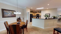 This single-story residence offers a thoughtfully designed layout that balances open communal spaces with comfortable private quarters. The kitchen serves as a functional centerpiece, featuring light maple cabinetry extending to the ceiling, dark granite countertops, black appliances including a refrigerator, dishwasher, and microwave, and a skylight that draws natural light into the space. Large-format tile flooring grounds the kitchen, which opens directly to the dining area via a peninsula with additional counter seating.

The dining area is defined by crown molding, a chair rail, and a chandelier pendant light, creating an intimate yet refined atmosphere. Soft carpet continues into the adjacent living room, where crown molding and neutral beige walls contribute to a cohesive, warm ambiance.

The bedrooms are carpeted and feature neutral walls, with windows dressed in panel curtains that allow natural light. The bathrooms are finished with large-format tile surrounds in earthy tones, featuring tub-shower combinations. A secondary bathroom includes a tiled tub surround with a curtain rod, a vanity with wood cabinetry, and tile flooring, maintaining a consistent design language throughout the home.