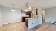 This single-floor residence is thoughtfully laid out to maximize functionality and comfort. The open-concept living and dining area is finished with light wood-look flooring and neutral gray walls, creating a bright, cohesive atmosphere. A wall of sliding glass doors leads to a private balcony overlooking a tree-lined outdoor setting, filling the space with natural light.

The kitchen is a standout feature, equipped with rich dark-stained cabinetry, granite countertops, and stainless steel appliances including a refrigerator and range. A peninsula with matching granite provides additional prep space and a natural division between the kitchen and living areas, complemented by a pendant light fixture overhead. A secondary kitchen configuration offers a galley-style layout with ample upper and lower cabinet storage.

The bedrooms are carpeted and generously sized, each featuring sliding windows with views of mature trees and baseboard heating units along the perimeter walls.

The bathrooms are well-appointed, showcasing dark wood vanities topped with granite counters, large mirrors, tile wainscoting, and classic mosaic tile flooring—providing a clean, polished finish throughout.