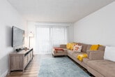 This single-floor residence offers a thoughtfully arranged layout that balances comfort and functionality across its living spaces. The living room serves as the heart of the home, featuring wood-look flooring, a textured ceiling, and a large sliding glass door dressed with vertical blinds that floods the room with natural light. The kitchen is outfitted with crisp white cabinetry, sleek brushed-nickel hardware, marble-look countertops, and stainless steel appliances, including a full-size refrigerator and range. Adjacent to the kitchen, the dining area provides a comfortable space for everyday meals. The residence includes multiple bedrooms, each carpeted for warmth and comfort. The primary bedroom features neutral tones and ample space, while a secondary bedroom doubles as a functional home office with a built-in desk setup and natural light from a window with blinds. A third bedroom includes a sliding-door closet and overhead lighting. The bathroom is clean and well-maintained, with a tub-shower combination, a striped shower curtain, and marble-look surfaces. Throughout, the neutral color palette and consistent flooring create a cohesive and welcoming atmosphere.