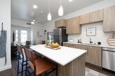 Located at 3040 S Fork Blvd in Idaho Falls, Idaho, this thoughtfully designed one-bedroom, one-bathroom unit offers a functional and stylish single-floor layout. The open-concept living and kitchen area serves as the heart of the unit, where light wood cabinetry, white quartz countertops, and a full suite of stainless steel appliances — including a refrigerator, dishwasher, range, and over-the-range microwave — create a modern and efficient kitchen. A central island with pendant lighting provides both additional prep space and casual seating. Wide-plank wood-style flooring runs throughout the main living areas, complementing the clean, neutral palette. The living room is bright and welcoming, featuring a ceiling fan, a private entrance with a glass-paned door that invites natural light, and enough space for comfortable seating and entertainment. The bedroom is carpeted for warmth and comfort, with ceiling fan, natural light from windows with shutters, and ample room for a full bedroom suite. The bathroom connects directly to the bedroom and includes a vanity with wood-tone cabinetry, a soaking tub, and clean white finishes. This unit offers a cohesive, modern aesthetic with practical design throughout.