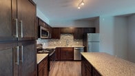 Located at 4000 SW Modern Way in Bentonville, Arkansas, this single-floor residence offers a thoughtfully designed layout with contemporary finishes throughout. The kitchen serves as a standout feature, showcasing rich dark-espresso cabinetry, granite countertops, a mosaic tile backsplash, and a full suite of stainless steel appliances including a refrigerator, range, microwave, and dishwasher. A central island provides additional prep and storage space, while wood-style flooring ties the area together with warmth and practicality. The bedrooms are carpeted for comfort and each is equipped with a ceiling fan and generously sized windows that invite natural light and exterior views. The primary bathroom is well-appointed with a granite-topped dark vanity, tile flooring, and direct access to a spacious walk-in closet fitted with wire shelving and hanging rods. A secondary bathroom mirrors the same quality finishes and also connects to an additional walk-in closet. Neutral gray tones are used consistently throughout the living spaces, creating a clean and cohesive aesthetic. The overall design balances modern style with functional living, making this Bentonville property a well-equipped and move-in ready residence.