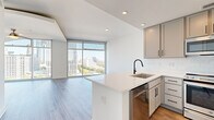 Located in the heart of Atlanta's prestigious Buckhead neighborhood at 3242 Peachtree Rd NE, this thoughtfully designed single-floor unit offers a bright, modern living experience. The open-concept layout connects the living room and kitchen seamlessly, anchored by dramatic floor-to-ceiling glass windows that flood the space with natural light and frame stunning panoramic views of the Atlanta skyline and lush treetop canopy below.

The living room is generously proportioned for its footprint, featuring light wood-tone flooring, a ceiling fan, and an arched soffit detail that adds architectural character. The kitchen is well-appointed with gray shaker-style cabinetry, black hardware accents, white quartz countertops, a white subway tile backsplash, and a full suite of stainless steel appliances including a range, microwave, dishwasher, and refrigerator. A peninsula with an undermount sink extends into the living area, ideal for casual dining or entertaining.

The bathroom offers a clean, contemporary finish with large-format tile flooring, a tiled soaking tub and shower combo, gray cabinetry, and recessed lighting. A hallway and closet provide practical storage solutions. Throughout the unit, recessed lighting and crisp white walls maintain a clean, modern aesthetic that complements the elevated urban views.
