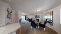 This single-floor residence offers a thoughtfully designed layout that seamlessly connects its primary living spaces. The open-plan living and dining area forms the heart of the unit, featuring neutral-toned carpet, a textured ceiling, and a ceiling fan overhead. A sliding glass door floods the living room with natural light and provides direct access to a private balcony with outdoor views of mature trees. The dining area is defined by a corner window that further enhances the sense of light and openness.

The galley-style kitchen is efficiently organized, featuring warm wood cabinetry, white countertops, hardwood-style flooring, and a full suite of appliances including a range, microwave, and refrigerator. A dedicated walk-in pantry offers generous storage. A breakfast bar connects the kitchen to the main living area.

The two bedrooms are carpeted and tranquil, with the primary bedroom featuring its own sliding glass door to an additional private balcony. A mirrored closet adds depth and practicality. The full bathroom includes a single vanity, a tub-shower combination, and hardwood-style flooring, maintaining a clean and functional aesthetic throughout.