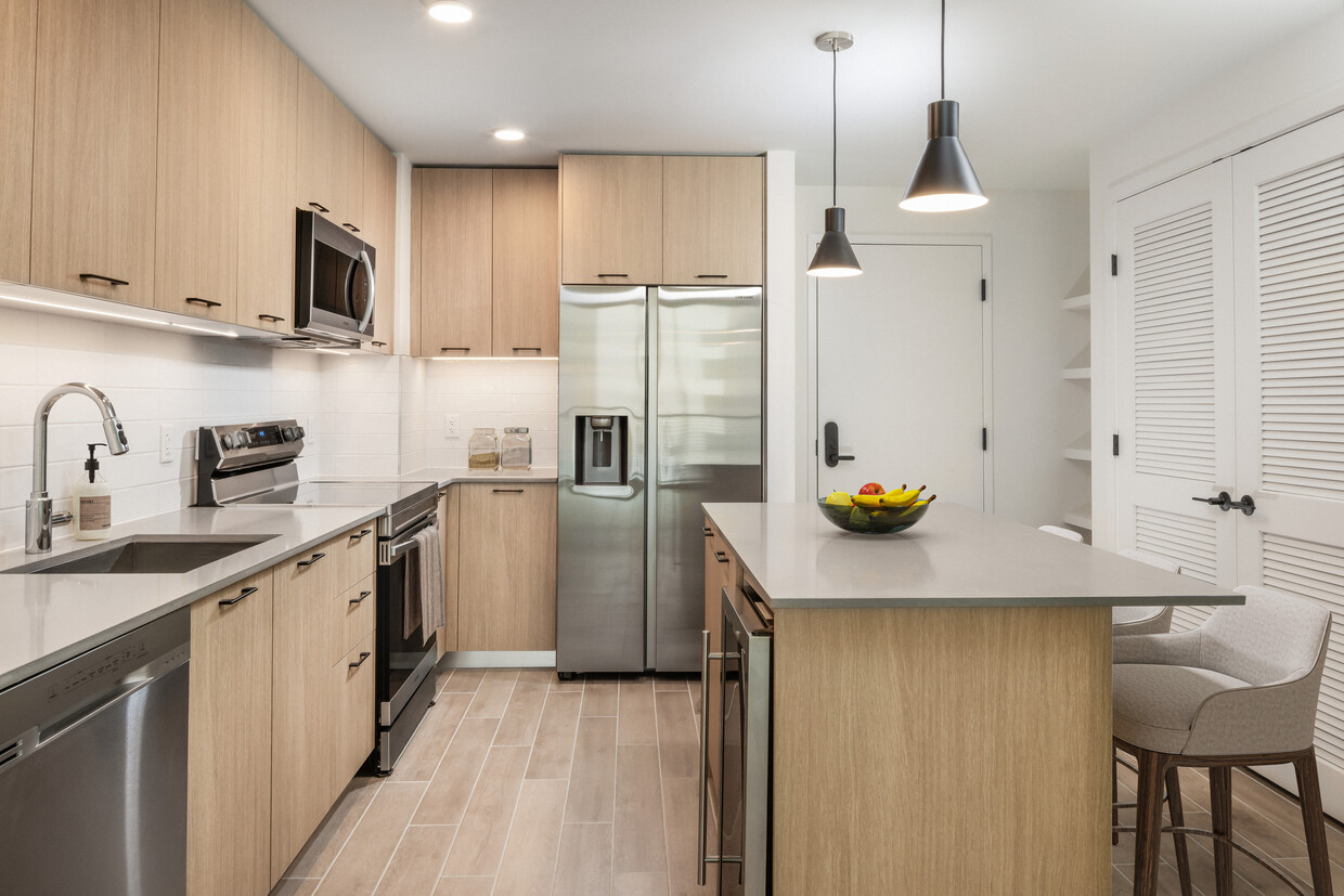 Cocina con electrodomésticos de acero inoxidable, encimeras de cuarzo gris, salpicadero de azulejos blancos y suelos de superficie dura - Avalon Merrick Park