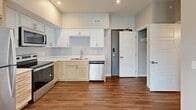 This efficiently designed 1-bedroom, 1-bathroom unit offers a thoughtful single-level layout that maximizes every square foot. The open-concept living and kitchen area forms the heart of the space, anchored by warm wood-style flooring that flows seamlessly throughout. Large windows and a sliding glass door leading to a private balcony flood the interior with natural light and provide pleasant outdoor views.

The kitchen is well-appointed with a mix of white shaker-style and light natural wood cabinetry, light-toned countertops, a stainless steel refrigerator, electric range, built-in microwave, and dishwasher — offering both style and practicality. The adjacent living area benefits from the open sightlines and balcony access, creating an airy, connected feel.

The bedroom is a comfortable, neutral-toned retreat with windows dressed in blinds and direct access to a dedicated walk-in closet with built-in shelving. The bathroom features a clean, all-white walk-in shower enclosure alongside standard fixtures. A hallway connects the main rooms efficiently, completing a well-organized floor plan. Neutral gray walls, recessed lighting in the kitchen, and consistent flooring throughout give the unit a cohesive, modern aesthetic.