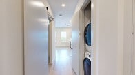Located at 1345 14th St in Plano, TX, this thoughtfully designed one-bedroom, one-bathroom unit offers a compact yet functional single-floor layout. The open kitchen is a standout feature, showcasing contemporary flat-panel cabinetry in a warm wood-tone finish, a white subway tile backsplash, light quartz countertops, and a full suite of stainless steel appliances including a range, microwave, dishwasher, and refrigerator. Large windows flood the kitchen and living area with natural light and provide views of the surrounding greenery, complementing the light hardwood flooring throughout the main living space. The bedroom offers a cozy, carpeted retreat with a sliding barn-style door that adds a modern touch, along with an electrical panel access point built into the wall. The bathroom features elegant marble-look floor-to-ceiling tile surrounding a soaking tub and shower combination, accented by matte black hardware and fixtures for a clean, contemporary aesthetic. Neutral tones and recessed lighting throughout the unit contribute to a bright, cohesive ambiance, making this a well-appointed space ideal for comfortable everyday living.