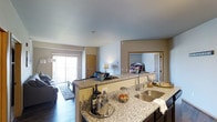 This single-floor residence on Shelby Avenue in Rapid City, South Dakota, offers an open-concept design that seamlessly integrates the kitchen, dining, and living areas into one cohesive space. The kitchen serves as a central hub, featuring a large island with granite countertops, a stainless steel sink, and dark cabinetry that provides a striking contrast to the light stone surfaces. The island offers generous prep and storage space, making it both functional and visually appealing.

The living area flows naturally from the kitchen, highlighted by hardwood-style flooring and neutral-toned walls that create a warm, welcoming atmosphere. Smooth, high ceilings enhance the sense of openness throughout. A sliding glass door in the living area fills the space with natural light and provides direct access to an outdoor area, extending the functional living space.

A bedroom is visible from the main living area, framed by a doorway with warm wood trim that ties the design elements together. The overall aesthetic throughout the home is modern and cohesive, combining neutral tones, quality finishes, and practical layouts suited for comfortable everyday living in Rapid City.