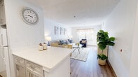 Located at Providence Village Drive in Sterling, Virginia, this single-floor, one-bedroom, one-bathroom residence offers a thoughtfully designed open-concept layout that maximizes its efficient footprint. Light-toned walls and wood-look flooring run throughout the main living areas, creating a bright and cohesive aesthetic.

The kitchen is well-equipped with gray shaker-style cabinetry, stainless steel appliances including a dishwasher, range, and microwave, complemented by a striking blue-and-white mosaic tile backsplash and white quartz countertops. A peninsula counter provides additional prep space and serves as a natural divider between the kitchen and living area.

The living room is open and inviting, bathed in natural light from a large window with a decorative valance. The entryway flows seamlessly into this space, highlighted by warm wood-look flooring and a textured accent wall.

The bedroom offers plush carpeting, a generously sized window with curtains, and two closets for ample storage. The bathroom features wood-look flooring, a white vanity with quartz countertop, a mirrored medicine cabinet, and clean, neutral finishes throughout. This residence combines practical functionality with a clean, modern aesthetic.