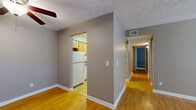 This single-floor residence offers a well-organized layout encompassing two bedrooms, two bathrooms, a living room, kitchen, hallway, and closet. The living room features warm hardwood-style flooring, neutral gray-toned walls, a ceiling fan, and a textured ceiling, with natural light entering through double windows fitted with blinds. The space connects directly to a hallway that links the remaining rooms.

The kitchen is equipped with light oak cabinetry, granite-style countertops, a white electric range with overhead ventilation, and a white refrigerator, all set atop tile flooring. The primary bedroom is generously proportioned with plush carpeting, neutral walls, and direct access to an en-suite bathroom featuring warm wood vanity cabinetry. The second bedroom also features carpet flooring, a window for natural light, and built-in shelving along one wall, along with a sizable closet with a hanging rod.

Both bathrooms are functional in design; one includes a full tub-shower combination with white tile surround, while the other features a tiled walk-in shower. Throughout the unit, consistent neutral tones and textured ceilings create a cohesive and practical living environment.