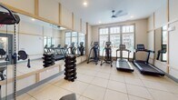 Located at 701 S Buncombe Rd in Greer, South Carolina, this fitness center is thoughtfully designed to support a comprehensive workout experience. The space is finished with large-format tile flooring throughout, neutral walls, and warm wood-toned trim accents that frame the room's large windows, flooding the interior with natural light and offering views of the surrounding community.

The cardio zone is well-appointed with multiple treadmills and elliptical machines positioned along the windowed wall, making workouts feel open and energizing. A ceiling fan overhead contributes to airflow and comfort during exercise. An expansive wall-mounted mirror runs the length of one side of the room, visually enlarging the space while allowing users to monitor their form. Flanking the mirror, a full dumbbell rack offers a range of free weights for strength training.

A dedicated cable machine with an adjustable bench, branded by BodyCraft, anchors the strength training area, providing versatile resistance options. A separate, quieter nook within the space features carpet flooring and a wall-mounted foldable mat, ideal for stretching, yoga, or recovery work. The fitness center is accessed through a glass-panel door and includes recessed lighting, creating a clean, modern atmosphere suitable for all fitness levels.