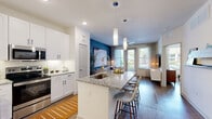 Located at Wells Creek Pkwy in Jacksonville, FL, this thoughtfully designed one-bedroom, one-bathroom residence offers a functional and stylish single-floor layout. The open-concept living area flows seamlessly into a modern kitchen equipped with stainless steel appliances, sleek white cabinetry extending to the ceiling, a subway tile backsplash, and a granite-topped island with bar seating — ideal for both meal preparation and casual dining. Warm hardwood-style flooring runs throughout, complementing the bright, neutral color palette. Recessed and pendant lighting add a refined touch to the kitchen and living spaces, which benefit from generous natural light through large windows. The bedroom is a comfortable retreat featuring a ceiling fan, large windows with outdoor views, and soft, neutral tones. It is complemented by a dedicated walk-in closet with built-in shelving and hanging storage. The bathroom offers a granite-topped vanity with a wide mirror, hardwood-style flooring, and direct access to the closet. A private balcony extends the living space outdoors, providing a personal outdoor area. The overall ambiance is clean, contemporary, and welcoming throughout.