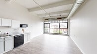 Located in the heart of downtown Dayton, Ohio, this urban loft-style unit at 35 S Saint Clair St, Unit 319, blends industrial character with modern comfort. The open living area is a standout, featuring floor-to-ceiling grid-pane windows that frame sweeping city views and flood the space with natural light. Exposed structural beams and large-diameter ductwork running across the ceiling reinforce the loft aesthetic, while light-toned hardwood-style flooring grounds the space in a clean, contemporary feel.

The kitchen is efficiently laid out with white cabinetry, light countertops, and black appliances including a refrigerator, electric range, dishwasher, and microwave. A dedicated walk-in closet area provides generous storage with high ceilings that continue the loft's vertical character.

The bedroom offers a quieter retreat with plush carpeting, high ceilings, and direct access to one of the two bathrooms. Both bathrooms are thoughtfully appointed with gray vanity cabinetry, single-basin sinks, large mirrors, and hardwood-style flooring. One bathroom features a stylish marble-patterned shower curtain, adding a decorative touch. Two hallways connect the layout efficiently, contributing to a functional and well-organized floor plan throughout this distinctive downtown residence.