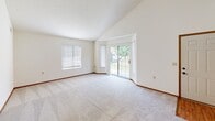 This single-floor residence offers a thoughtfully designed layout with a variety of functional spaces. The main living area immediately impresses with its dramatic vaulted ceilings, which lend an airy, open feel to the room. Soft carpeting runs throughout the living and bedroom areas, complemented by warm wood-toned baseboards that provide a cohesive aesthetic. Large sliding glass doors in the living room invite abundant natural light and offer views of the greenery outside, while an additional window further brightens the space.

The kitchen is well-appointed with warm wood cabinetry, light stone-toned countertops, and black appliances including an electric range and an over-the-range microwave. The kitchen opens toward the main living area, making it ideal for everyday living. Hardwood-style flooring in the entryway and kitchen provides a practical contrast to the carpeted areas.

The bedrooms are comfortably sized, each featuring neutral walls, plush carpet, and windows fitted with horizontal blinds for privacy and light control. An accessible bathroom rounds out the unit, equipped with stainless steel grab bars near the toilet, wood-toned cabinetry, a vanity with ample storage, and durable hardwood-style flooring — a detail that underscores the unit's commitment to accessibility and ease of use throughout.