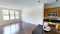 This single-floor unit is designed with a clean, modern aesthetic that maximizes its well-proportioned footprint. The open-concept living and dining area features rich, dark hardwood-style flooring that runs throughout, creating a warm and cohesive feel. Crisp white walls provide a neutral backdrop, while a stylish pendant light fixture serves as a subtle focal point overhead. A window along the exterior wall allows natural light to filter into the living space, brightening the interior.

The kitchen flows directly from the living area, featuring dark granite countertops that contrast with warm wood-toned cabinetry. This layout promotes an efficient use of space while maintaining an open connection between cooking and living areas. The unit includes one bedroom and one full bathroom, offering a practical and comfortable configuration. Ceiling-mounted HVAC vents ensure year-round climate control. Overall, the unit presents a straightforward, well-maintained interior with functional finishes suited for everyday living.