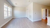 Located at 104 Washington Street in downtown Dover, New Hampshire, this efficiently designed single-floor unit offers a thoughtfully arranged layout that maximizes every square foot. The open-concept kitchen and living area serves as the heart of the space, showcasing a modern kitchen with two-tone cabinetry — white upper cabinets paired with charcoal lower cabinets — complemented by light quartz countertops, a subway tile backsplash, and a full suite of stainless steel appliances including a refrigerator, range, microwave, and dishwasher. A peninsula with a built-in sink and pendant lighting overhead provides both additional prep space and a natural division between the kitchen and living area. The living area benefits from generous natural light, courtesy of large windows and a sliding glass door that opens to views of the surrounding streetscape. Light wood-style flooring runs throughout the unit, lending a clean, cohesive aesthetic. The bathroom features a white vanity with quartz countertop, built-in open shelving, a large mirror, and a glass-enclosed walk-in shower. A dedicated laundry room includes a stacked washer and dryer unit along with wire shelving for added storage convenience.