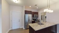 This single-floor residence is thoughtfully designed with an open-concept layout that seamlessly connects the living, dining, and kitchen areas. Wide-plank hardwood flooring runs throughout the main living spaces, complemented by neutral walls and recessed lighting that create a bright, cohesive atmosphere. A fireplace serves as a focal point in the living area, adding warmth and character to the space.

The kitchen is well-equipped with rich dark-stained cabinetry, granite countertops, and a full suite of stainless steel appliances, including a French door refrigerator, electric range, and built-in microwave. A central island with a granite surface and undermount sink provides additional workspace and casual seating. Pendant lighting above the island adds a refined finishing touch.

The dining area features a chandelier and windows that allow natural light to filter in. Bedrooms are carpeted for comfort, with at least one room offering sliding door access to a private outdoor balcony. A well-organized walk-in closet features built-in shelving, hanging rods, and a drawer unit. The bathroom includes a single-sink vanity with quartz countertop and a full tub-shower combination with brushed nickel fixtures. A dedicated laundry area houses a stacked washer and dryer unit with adjacent folding counter space.