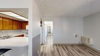 This single-floor unit offers a well-organized layout with consistent light wood-style laminate flooring running throughout every room, creating a cohesive and airy feel. The kitchen is a standout feature, equipped with warm honey-toned wood cabinetry, a speckled quartz countertop, a built-in sink, white appliances including a range, microwave, and refrigerator, and a breakfast bar with seating for two. A skylight-style overhead fixture brightens the cooking area naturally.

The living and hallway areas are open and connected, with a textured popcorn ceiling and neutral gray-toned walls that lend a calm, modern ambiance. The bedrooms are generously sized, each featuring plantation shutters that allow for adjustable natural light, textured ceilings, and individual climate control units. One bedroom includes a gold-framed mirrored sliding closet door, adding a reflective, space-enhancing detail. Ceiling fans with integrated lighting are present in select rooms for added comfort.

The bathroom is clean and functional, featuring a full tub-shower combo with a curved chrome rod and handheld showerhead, complemented by granite-style countertops and matching chrome fixtures. The overall space presents a tidy, move-in-ready environment with a neutral palette throughout.