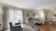 Located at 2210 Sullivan Rd in College Park, GA, this two-bedroom, one-bathroom residence offers a thoughtfully laid-out single-floor plan with a cohesive, neutral design palette throughout. The living room serves as the heart of the home, featuring rich hardwood flooring, a textured ceiling, and a large sliding glass door framed by vertical blinds and patterned accent curtains that flood the space with natural light and provide outdoor views. The adjacent dining area is defined by a pendant light fixture overhead and connects seamlessly to the kitchen, creating an open, functional flow. The kitchen is outfitted with white cabinetry, ample counter space, a stainless steel sink, a dishwasher, and a range, with a window that brings in additional natural light. The primary bedroom offers a comfortable, carpeted retreat with access to a hallway leading to the full bathroom. The second bedroom, also carpeted, provides a cozy and versatile space suitable for various uses. The full bathroom includes a tub-shower combination, a vanity with storage, and warm hardwood-style flooring. Soft gray tones on the walls carry consistently through each room, giving the home a clean, unified aesthetic throughout.