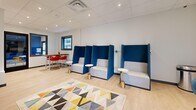 The Study at 801 Camino del Rio in Durango, Colorado, is a purposefully designed collaborative workspace that blends functionality with contemporary style. The single-floor layout is efficiently organized into distinct zones, each catering to different working and social needs.

The main lounge area features a row of tall-backed, high-privacy seating pods upholstered in bold navy blue and light gray, each paired with a compact round side table on a brushed gold base — ideal for focused individual work or quiet conversations. A geometric, multicolored area rug anchors the space, adding a lively visual element against the light wood-toned flooring throughout.

A high-top table with vibrant red bar stools provides a more social seating option, positioned beneath a large dark-framed window that brings in natural light. A sliding barn-style door in sage green, decorated with hexagonal accents, adds a charming architectural detail and separates a semi-private alcove.

The corridor area features floor-to-ceiling glass panels that open views to a lush outdoor courtyard, flooding the space with natural light. A built-in counter with bar seating offers additional workspace along this passageway. Bold blue accent walls and recessed lighting contribute to the space's modern, energetic atmosphere, making The Study a dynamic environment suited for productivity and community.
