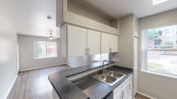 Located near I-25 in Westminster, Colorado, this single-story unit offers a practical and well-designed layout suited for comfortable everyday living. The kitchen serves as a central highlight, featuring white shaker-style cabinetry, dark granite-style countertops, a double stainless steel sink, and a full suite of stainless steel appliances including a refrigerator, electric range, and dishwasher. A peninsula counter provides additional workspace and creates a natural division between the kitchen and the adjoining living area, which is finished with wood-look flooring and benefits from natural light through a window overlooking the surrounding community. The bedroom is carpeted for warmth and comfort, offering a spacious feel with a dedicated closet featuring built-in shelving and hanging rods. The bathroom is finished with wood-look flooring, a white vanity with dark countertop, a wall-mounted mirror, and a full tub and shower combination with white tile surround. Throughout the unit, a neutral gray color palette, white trim, and consistent finishes create a clean, cohesive aesthetic. The entryway provides a smooth transition into the main living spaces.
