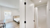 Located at 3001 Van Buren Place in Los Angeles, CA, this efficiently designed one-bedroom, one-bathroom unit offers a clean, modern aesthetic throughout its single floor. The interior is characterized by a bright, all-white palette paired with light wood-toned luxury vinyl flooring that runs seamlessly across every room, creating a cohesive and airy feel.

The bedroom is a comfortable, well-proportioned space featuring a window that brings in natural light, recessed ceiling lighting, and a built-in wardrobe providing practical storage. The room's minimalist design keeps the focus on functionality and openness.

A narrow hallway connects the bedroom to the entrance, with recessed lighting overhead and a window at the far end that draws the eye and adds depth to the corridor. A wooden desk-style surface along the hall offers a flexible workspace or utility area.

The bathroom is finished with contemporary fixtures, including a vessel sink atop a gray vanity with a white countertop, brushed chrome hardware, a backlit mirror, and light wood-tone flooring that mirrors the rest of the unit. A shower with a white curtain and a standard toilet complete the space.

Throughout, the unit's design prioritizes clean lines, neutral tones, and thoughtful use of every square foot, making it a practical and stylish option in the Los Angeles area.