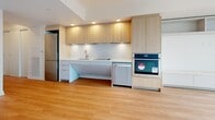 This well-designed 1-bedroom, 1-bathroom unit offers a thoughtfully organized layout across a single floor, making efficient use of its compact footprint. Light wood laminate flooring flows consistently throughout the living areas, hallway, and bedroom, creating a warm and cohesive aesthetic against the crisp white walls and ceilings.

The open-concept living and kitchen area is a standout feature, anchored by floor-to-ceiling windows that flood the space with natural light and provide views of the surrounding urban environment. The modern kitchen is outfitted with light wood flat-panel cabinetry, a wall-mounted oven, stainless steel refrigerator, dishwasher, and a sleek induction cooktop set into a clean white countertop — all arranged in an efficient galley-style configuration.

A long hallway connects the main living area to the bedroom and bathroom, with a sliding door offering practical storage access. The bedroom is a generously proportioned retreat featuring built-in closet doors and additional windows that bring in natural light. The bathroom is finished with large-format light tile flooring, a floating wood-toned vanity with an illuminated mirror, and a glass-enclosed walk-in shower, all contributing to a clean, contemporary aesthetic throughout.