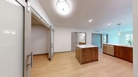 Located in Seattle's desirable Queen Anne neighborhood, this well-designed 2-bedroom, 1-bathroom residence offers a thoughtful layout across a single floor. Light wood-tone flooring runs throughout, creating a warm and cohesive aesthetic.

The open-concept kitchen and living area serves as the heart of the home. The kitchen is outfitted with rich walnut-toned cabinetry, white quartz countertops, a subway tile backsplash, and a full suite of stainless steel appliances including a range, microwave, refrigerator, and dishwasher. A central island with additional storage provides extra prep space and casual seating. Pendant lighting and recessed fixtures illuminate the area, while a wall-mounted mini-split unit offers efficient climate control.

The living room benefits from large sliding glass doors that invite abundant natural light and open to views of the surrounding Seattle streetscape and greenery. The primary bedroom similarly features an oversized window with scenic neighborhood views. The second bedroom includes its own wall-mounted climate unit and direct access to a dedicated walk-in closet with built-in wire shelving.

The bathroom is clean and modern, featuring a full soaking tub with shower, a long dual-sink vanity with walnut cabinetry, and a large mirror. A stylish sliding barn door adds a distinctive architectural touch to the main living space.