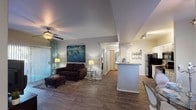 Located at 2222 N McQueen Rd in Chandler, Arizona, this single-story residence offers a well-designed, open-concept layout that maximizes both functionality and comfort. The living area is the heart of the home, featuring wood-style plank flooring, a ceiling fan, and a large sliding glass door dressed with vertical blinds and patterned curtains that allow abundant natural light to fill the space. The open sightlines connect the living room seamlessly to the kitchen, creating an inviting, communal atmosphere.

The galley-style kitchen is efficiently designed with ample white cabinetry, stone-tone countertops, a stainless steel sink, and black appliances including a refrigerator and electric range. Track lighting overhead ensures the workspace is well-lit throughout the day.

The bedrooms offer a relaxing retreat, each equipped with ceiling fans, plush carpeting, and windows that bring in natural light. The primary bedroom includes an en-suite bathroom and generous closet space.

Both bathrooms are finished with white cabinetry, stone-tone countertops, large mirrors, and tub-shower combinations with full-length curtains. Wood-style flooring carries through these spaces for a cohesive aesthetic. The overall design balances practicality with a clean, contemporary style throughout.