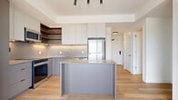 This contemporary 2-bedroom, 2-bathroom residence at 280 Montgomery Street in Ottawa offers a thoughtfully designed open-concept layout finished with modern materials throughout. Light hardwood flooring flows seamlessly across the main living areas, enhancing the bright, airy atmosphere created by large floor-to-ceiling windows and a balcony door that frame sweeping views of the Ottawa skyline and surrounding greenery.

The kitchen is a standout feature, outfitted with sleek two-tone cabinetry in white and grey, warm wood open shelving, a grid-tile backsplash, stone countertops, stainless steel appliances including a built-in microwave and refrigerator, and a central island that doubles as a breakfast bar. The kitchen flows directly into the combined dining and living area, making the space ideal for both daily living and entertaining.

The primary bedroom is generously proportioned and benefits from expansive windows with balcony access, flooding the room with natural light and city views. Both bedrooms are equipped with mirrored sliding closet doors. The two bathrooms are finished with grey tile wainscoting, stone-topped vanities, and matte black fixtures — one featuring a soaker tub and the other a glass-enclosed walk-in shower. A dedicated laundry area and ample closet storage complete this well-appointed home.