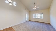 This single-story, one-bedroom, one-bathroom unit offers a thoughtfully organized layout that maximizes its compact footprint. The living room immediately stands out with its dramatic vaulted ceiling, which lends a sense of openness well beyond its physical dimensions. A ceiling fan with integrated lighting anchors the space, while a wide multi-pane window and a glass-paneled exterior door flood the room with natural light. Soft carpeting covers the living area floor, adding warmth underfoot.

The kitchen is efficiently designed, featuring warm honey-toned wood cabinetry, a tile backsplash, granite-look countertops, and white appliances including a refrigerator, electric range with overhead microwave, and a double basin sink. Adjacent to the kitchen is a dedicated closet equipped with wire shelving and washer/dryer hookups, adding practical utility.

The bedroom is a comfortable, well-proportioned space with carpeting, a ceiling fan, and a window that brings in exterior views and natural light. A closet provides storage within the room.

The bathroom offers a full tub-shower combination with a curved curtain rod, a single-sink vanity with wooden cabinetry, and wood-look vinyl flooring, completing this functional and cohesive unit.
