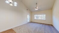 This single-story, one-bedroom, one-bathroom unit offers a thoughtfully organized layout that maximizes its compact footprint. The living room immediately stands out with its dramatic vaulted ceiling, which lends a sense of openness well beyond its physical dimensions. A ceiling fan with integrated lighting anchors the space, while a wide multi-pane window and a glass-paneled exterior door flood the room with natural light. Soft carpeting covers the living area floor, adding warmth underfoot.

The kitchen is efficiently designed, featuring warm honey-toned wood cabinetry, a tile backsplash, granite-look countertops, and white appliances including a refrigerator, electric range with overhead microwave, and a double basin sink. Adjacent to the kitchen is a dedicated closet equipped with wire shelving and washer/dryer hookups, adding practical utility.

The bedroom is a comfortable, well-proportioned space with carpeting, a ceiling fan, and a window that brings in exterior views and natural light. A closet provides storage within the room.

The bathroom offers a full tub-shower combination with a curved curtain rod, a single-sink vanity with wooden cabinetry, and wood-look vinyl flooring, completing this functional and cohesive unit.