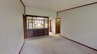 This single-floor, 2-bedroom, 2-bathroom residence in Plymouth, Michigan offers a practical and functional layout throughout. The living area is carpeted and connects to the kitchen via a distinctive open shelving and cabinet divider, complete with dark wood framing and built-in lower storage — a hallmark architectural detail that defines the space. The kitchen is efficiently arranged with white cabinetry accented by dark wood trim, a butcher block-style countertop, a stainless steel sink, an electric range, and a refrigerator, all set on tile flooring with ample cabinet storage above and below. Both bedrooms are generously sized, featuring plush carpeting, textured wallpaper, ceiling fans with light fixtures, windows overlooking outdoor greenery, and baseboard heating units. The two full bathrooms each include a tub-shower combination and toilet; one features wood-look vinyl flooring with a marble-style vanity countertop, while the other has classic tile flooring. A dedicated laundry room with wood-look flooring houses the water heater and washer/dryer connections, adding everyday convenience. The living area also provides direct outdoor access through a glass door, bringing in natural light and views of the surrounding landscape.