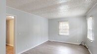 This single-story home offers five bedrooms and two bathrooms within a thoughtfully arranged floor plan. The interior is finished with a consistent light gray and white color palette throughout, creating a clean and cohesive aesthetic. Wood-look luxury vinyl flooring runs through the main living areas, hallways, kitchen, and select bedrooms, while plush carpeting is featured in several of the bedrooms for added comfort.

The living area is bright and open, featuring two windows with blinds that allow ample natural light to fill the space, complemented by a textured ceiling and crown molding. The kitchen is well-equipped with white cabinetry, dark granite-style countertops, and stainless steel appliances including a refrigerator, range, and dishwasher. A window above the sink area adds natural light to the workspace.

The five bedrooms vary in size, with the primary bedroom offering a generous footprint. Each room features neutral walls and windows with blinds. One bedroom includes carpet flooring and a ceiling light fixture, while others showcase the wood-look flooring.

The two bathrooms serve the home effectively — one includes a bathtub and shower combination, while the other features a single vanity with mirror, toilet, and wood-look flooring. Two hallways connect the rooms, and a dedicated closet provides additional storage.