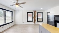 Located at 511 Maple Blvd in Kansas City, MO, this one-bedroom, one-bathroom unit offers a thoughtfully designed layout across a single floor. Light-toned luxury vinyl plank flooring runs throughout, lending a clean, cohesive look to every room.

The kitchen serves as the heart of the unit, featuring gray cabinetry, dark countertops, a stainless steel sink, and a full suite of black appliances including a refrigerator, gas range, microwave, and dishwasher. A freestanding gray kitchen island with a butcher block top adds extra prep and storage space. An exposed brick accent wall adds a touch of character and historic charm. In-unit laundry is conveniently located adjacent to the kitchen area.

The bedroom is bright and airy, with a large picture window framed in black that fills the room with natural light and offers views of the surrounding greenery. A ceiling fan with integrated lighting provides both comfort and functionality. The white walls and light flooring keep the space feeling open and fresh.

The bathroom features a clean, all-white walk-in shower enclosure with built-in corner shelving and chrome fixtures, maintaining the unit's modern and minimalist aesthetic throughout.