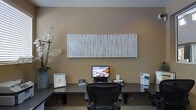 This single-floor professional space presents a refined and contemporary work environment designed with both function and aesthetics in mind. The focal point of the space is a streamlined workstation featuring a wide, dark-surfaced desk paired with an ergonomic task chair, creating an efficient and comfortable workspace. A desktop computer monitor sits centrally on the desk alongside neatly arranged informational materials and framed signage, suggesting a reception or client-facing function.

Above the workstation, a large-format textured wall panel in white and silver tones serves as a striking decorative element, adding depth and artistic interest to the warm beige wall behind it. The piece draws the eye upward and contributes to the space's polished, upscale character.

To the left, a tall arrangement of white orchids in a modern container introduces a touch of natural elegance, softening the otherwise clean and minimal aesthetic. The overall color palette — warm neutrals, dark accents, and crisp whites — creates a cohesive and professional atmosphere.

The space is thoughtfully appointed and well-organized, conveying a sense of calm and order suited to a business or professional services environment. The design balances practicality with tasteful décor, making it welcoming and highly functional for both staff and visitors.