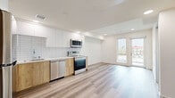 Located at 3170 W Olympic Blvd in Los Angeles, CA, this modern one-bedroom, one-bathroom unit offers a well-designed layout with contemporary finishes throughout. Light wood-look flooring runs continuously across the entire space, creating a cohesive and clean aesthetic.

The kitchen is a standout feature, equipped with a full suite of stainless steel appliances including a refrigerator, electric range, over-the-range microwave, and dishwasher. Two-tone cabinetry pairs white upper cabinets with warm wood-finish lower cabinets, complemented by a white subway tile backsplash and light countertops, delivering a fresh, modern look.

The spacious bedroom offers a generous footprint with recessed lighting, a large mirrored sliding-door closet, and a sizable window framing views of the Los Angeles skyline, filling the room with natural light and a sense of openness.

The bathroom features a soaking tub with a showerhead, floor-to-ceiling grey tile surround, a wood-finish storage tower, and a vanity, all tied together by the consistent wood-look flooring. A balcony provides additional outdoor space. The unit's clean lines, neutral palette, and modern finishes make it a bright and functional urban residence.