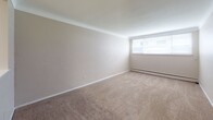 Located at 621 Larpenteur Ave W in Roseville, Minnesota, this single-floor unit offers a straightforward, functional layout well-suited for everyday living. The floor plan, visible in the 3D overview, reveals a logical arrangement of spaces that flow from the main living area through to the private rooms and utility spaces.

The living area is generously proportioned, featuring neutral-toned carpet, smooth walls, and a large window that allows natural light to fill the room. A baseboard heating system runs along the perimeter, providing efficient warmth throughout the colder months. The space opens toward a pass-through kitchen, which is equipped with white cabinetry, a coil-burner electric range, a full-size refrigerator, and tile flooring. The pass-through design connects the kitchen visually to the living space while maintaining a defined cooking area.

The bedroom is similarly finished with carpet flooring, neutral walls, a window for natural light, and baseboard heating. A ceiling-mounted light fixture provides consistent overhead illumination.

The bathroom features classic yellow ceramic tile on the lower walls and a mosaic tile floor, complemented by a white vanity with storage, a mirrored medicine cabinet, a tub-shower combination, and a wall-mounted light bar above the mirror. The overall ambiance of the unit is clean, practical, and move-in ready.