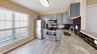 Located at 13 Harbison Way in Columbia, SC, this single-story residence offers a thoughtfully designed layout with a cohesive blend of modern finishes and comfortable living spaces. The kitchen serves as a functional centerpiece, showcasing granite countertops, gray shaker-style cabinetry, and a full suite of stainless steel appliances, including a range, over-the-range microwave, and refrigerator. A dark subway tile backsplash adds a striking contrast to the lighter cabinetry, while wood-look plank flooring grounds the space with warmth and durability. Natural light enters through a window adjacent to the kitchen area, keeping the space bright and inviting.

The living areas feature neutral-toned carpet, ceiling fans, and windows dressed with horizontal blinds, allowing for comfortable light control. The overall color palette throughout the home consists of warm beige tones that lend a clean, consistent feel from room to room. The bathroom includes wood-look flooring, a dark-toned vanity, and a window that introduces natural light. The open-concept flow between the kitchen and main living area, as visible in the floor plan model, supports an efficient and connected single-floor layout suited for everyday living.