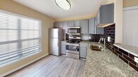 Located at 13 Harbison Way in Columbia, SC, this single-story residence offers a thoughtfully designed layout with a cohesive blend of modern finishes and comfortable living spaces. The kitchen serves as a functional centerpiece, showcasing granite countertops, gray shaker-style cabinetry, and a full suite of stainless steel appliances, including a range, over-the-range microwave, and refrigerator. A dark subway tile backsplash adds a striking contrast to the lighter cabinetry, while wood-look plank flooring grounds the space with warmth and durability. Natural light enters through a window adjacent to the kitchen area, keeping the space bright and inviting.

The living areas feature neutral-toned carpet, ceiling fans, and windows dressed with horizontal blinds, allowing for comfortable light control. The overall color palette throughout the home consists of warm beige tones that lend a clean, consistent feel from room to room. The bathroom includes wood-look flooring, a dark-toned vanity, and a window that introduces natural light. The open-concept flow between the kitchen and main living area, as visible in the floor plan model, supports an efficient and connected single-floor layout suited for everyday living.