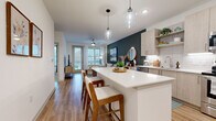 Located at 9821 Research Drive in Charlotte, NC, this thoughtfully designed one-bedroom, two-bathroom unit offers a modern and cohesive living experience across a single floor. The open-concept layout seamlessly connects the kitchen and living room, creating an inviting, functional space. The kitchen is outfitted with light wood cabinetry, white subway tile backsplash, stainless steel appliances — including a range, microwave, dishwasher, and refrigerator — and a white quartz island with bar seating, illuminated by stylish pendant lights. The living room features warm hardwood-style flooring, a bold teal accent wall, a ceiling fan, and large windows with a glass balcony door that fill the space with natural light and offer outdoor views. The bedroom is a comfortable retreat highlighted by a striking decorative wallpapered accent wall, a large window, and direct access to a well-appointed en-suite bathroom. The primary bathroom includes a light wood vanity, quartz countertop, soaking tub, and tiled shower. A second full bathroom and a dedicated laundry room with a stacked washer/dryer unit and wire shelving add practicality. Throughout, the design maintains a clean, contemporary aesthetic with neutral tones and quality finishes.