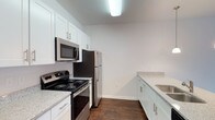 This single-floor 1-bedroom, 1-bathroom residence in Bluemont is thoughtfully designed to maximize comfort and functionality. The kitchen is a standout feature, showcasing crisp white shaker-style cabinetry with brushed nickel hardware, granite-look countertops, and a full suite of stainless steel appliances, including an electric range, over-the-range microwave, and refrigerator. Rich, dark hardwood-style flooring runs throughout the kitchen, grounding the space with warmth and contrast against the bright white cabinetry and clean white walls. The layout provides ample counter space and storage, making it well-suited for everyday cooking and entertaining. The overall interior palette is light and neutral, creating a clean, modern ambiance that feels open and inviting. The single-floor plan ensures easy accessibility and a seamless flow between living areas. With its updated finishes and efficient use of space, this Bluemont residence offers a practical yet stylish living environment suited for individuals or couples seeking a well-appointed home.