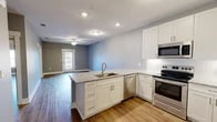 Located at Grand Park Lane in Thomasville, Georgia, this well-appointed one-bedroom, one-bathroom unit offers a thoughtfully designed layout across a single floor. The open-concept kitchen and living area serves as the heart of the home, where crisp white cabinetry, granite countertops, a peninsula with an undermount sink, and a full suite of stainless steel appliances — including a range, microwave, dishwasher, and French door refrigerator — create a functional and attractive kitchen space. Wood-style flooring flows seamlessly throughout the entire unit, lending warmth and visual continuity. The living area is accented by a ceiling fan and receives natural light through a glass exterior door. The bedroom offers a comfortable, well-sized retreat with a ceiling fan, a natural light window, and a closet with built-in shelving. The bathroom is clean and practical, featuring a walk-in shower with grab bar, a toilet, and matching wood-style flooring. Additional features include a utility area and an entry foyer. Neutral gray walls throughout create a calm, modern palette, making the space feel bright and move-in ready.
