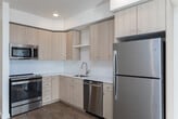 Located at 13450 W Baldcypress St in Boise, Idaho, this one-bedroom, one-bathroom unit offers a thoughtfully designed single-level layout filled with natural light and contemporary finishes throughout. The open-concept living and kitchen area is anchored by warm hardwood-style flooring that extends seamlessly from room to room. The kitchen is well-appointed with light wood cabinetry, white quartz-style countertops, a classic white tile backsplash, and a full suite of stainless steel appliances including a refrigerator, range, microwave, and dishwasher. A stainless steel undermount sink with a pull-down faucet adds a polished touch. The living area is bright and airy, with a glass-paned door leading to an outdoor space, allowing ample natural light to flow in. The bedroom features plush carpeting, a generous window with exterior views, a wall-mounted climate control unit, and access to a closet. The bathroom is clean and functional, offering a full tub-shower combination with tiled surround, a light wood vanity with a white countertop, and a large mirror. Recessed lighting throughout the unit enhances the modern, welcoming ambiance of this well-finished Boise residence.