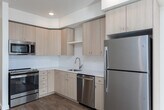 Located at 13450 W Baldcypress St in Boise, Idaho, this one-bedroom, one-bathroom unit offers a thoughtfully designed single-level layout filled with natural light and contemporary finishes throughout. The open-concept living and kitchen area is anchored by warm hardwood-style flooring that extends seamlessly from room to room. The kitchen is well-appointed with light wood cabinetry, white quartz-style countertops, a classic white tile backsplash, and a full suite of stainless steel appliances including a refrigerator, range, microwave, and dishwasher. A stainless steel undermount sink with a pull-down faucet adds a polished touch. The living area is bright and airy, with a glass-paned door leading to an outdoor space, allowing ample natural light to flow in. The bedroom features plush carpeting, a generous window with exterior views, a wall-mounted climate control unit, and access to a closet. The bathroom is clean and functional, offering a full tub-shower combination with tiled surround, a light wood vanity with a white countertop, and a large mirror. Recessed lighting throughout the unit enhances the modern, welcoming ambiance of this well-finished Boise residence.